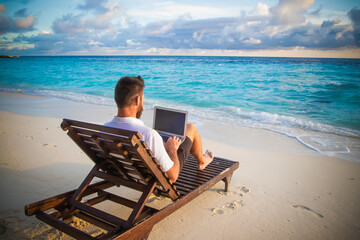 man working on laptop on tropical beach