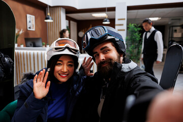 Beautiful couple enjoying winter holiday at ski resort, dressed in winter gear, taking pictures...