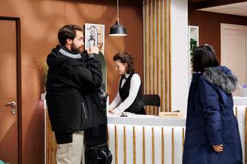 Youthful man and woman at front desk being assisted with check-in by friendly hotel receptionist....
