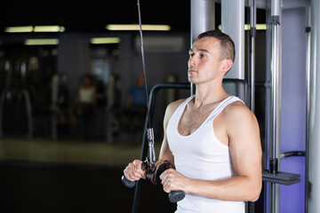 Young athletic man in sportswear training with straps in gym