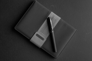 Black notebook with pen on black background. Top view.
