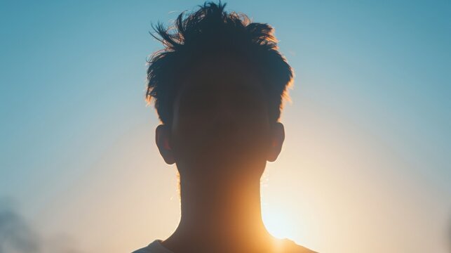 Silhouetted portrait of a person against a vibrant sunset sky. Backlit, with tousled hair and serene atmosphere. Perfect for themes of introspection, tranquility, and natural beauty.