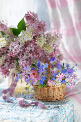 Spring still life with flowers, a bouquet of blooming lilacs and bird cherry in a vase, a basket with pansies, forget-me-nots and phlox, a beautiful postcard.