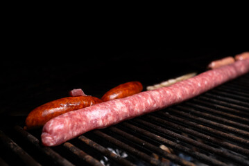 Some beef and pork sausages are cooked on a barbecue. Sausages, chorizo, and bacon are a rich but...
