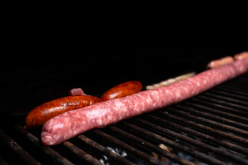 Some beef and pork sausages are cooked on a barbecue. Sausages, chorizo, and bacon are a rich but unhealthy food