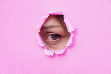 A woman's eye looking through torn pink paper. copy space for text