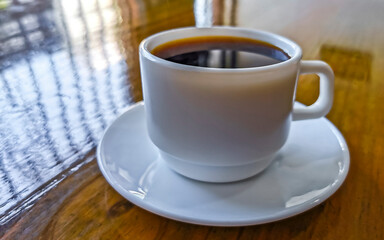 White cup of black Americano coffee on a wooden table.