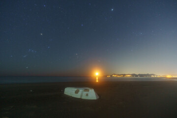 Beach with white boat and illuminated Amalfi Coast at hazy night with Orion and Pleiades...