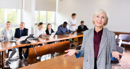 Smiling elegantly dressed elderly white female entrepreneur standing in boardroom at office, posing...