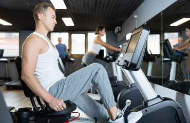 Young athletic man in sportswear training on exercise bike in gym