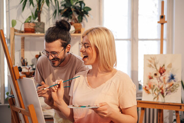 Fototapeta premium Young happy painters creating artwork on easel in creative studio.