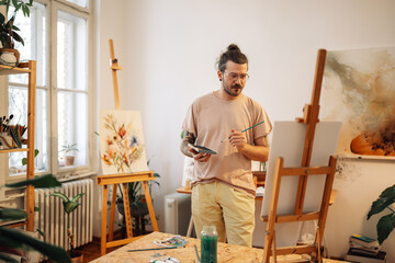 Portrait of focused artist with brush and palette looking at artwork.