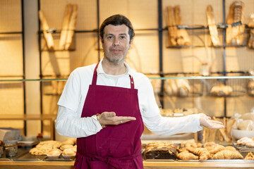 Positive adult bakery salesman in apron looking at the camera during working day in bakehouse....