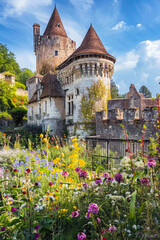 Medieval castle and flower garden in summer, vertical view old houses, sky and green plants. Theme of nature, travel, gothic