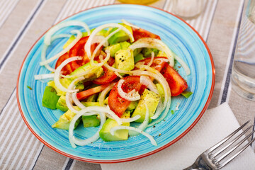 Tomato, avocado, onion salad cooked and served on table in restaurant.