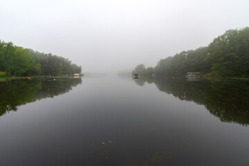 Looking  onto a calm Wisconsin lake on a foggy morning.  Fishing boat in distance.