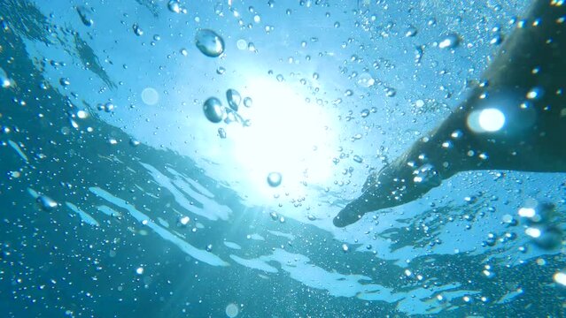 POV UNDERWATER, LENS FLARE: Drowning person in despair tries to swim to the sea surface to get some air. Bubbles in crystal clear blue sea with flailing hands frantically reaching back out of water.