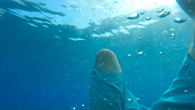 POV UNDERWATER: Male swimmer desperately tries to swim back above sea surface to get some air before drowning. Unrecognizable man frantically flailing his arms and legs to float out of the water.