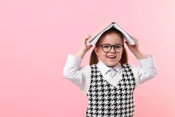 Cute little girl in glasses with open book on pink background. Space for text