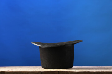 Magician's hat on wooden table against blue background, space for text