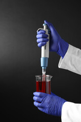 Laboratory analysis. Scientist dripping sample with micropipette into beaker on dark background,...