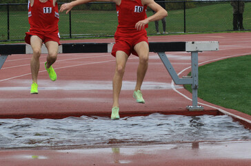 Two runners jumping into the water during a steeplechase track runners race