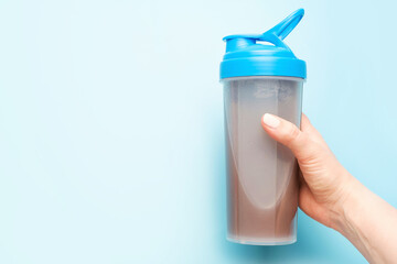 Hand holds a shaker with a protein shake on blue background.