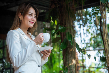 Woman drinking coffee hands holding hot disposable cup in green park. Happy Relax beautiful asian woman smiling face standing outdoors garden. Young women enjoy nature morning Freedom Lifestyle.