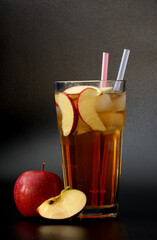 A tall glass of fresh apple juice with ice and pieces of ripe fruit on a black background.