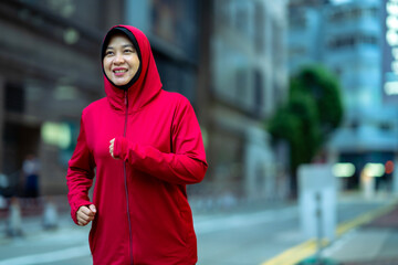 Glad smiling young asian muslim female in hijab with fitness tracker running on building background outdoor. Fitness outside, jogging in morning, body and health care, training, concept muslim sport.