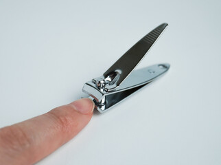 Human finger on stainless steel chrome metal iron small travel sized nail trimmer or clipper. Object photography isolated on white background.