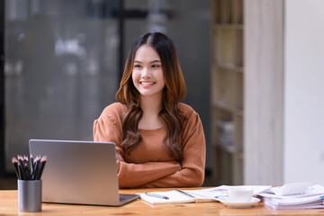 A young woman sitting in a nice pose at working desk in front of a laptop in the office.