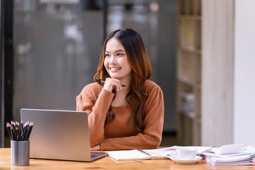 A young woman sitting in a nice pose at working desk in front of a laptop in the office.