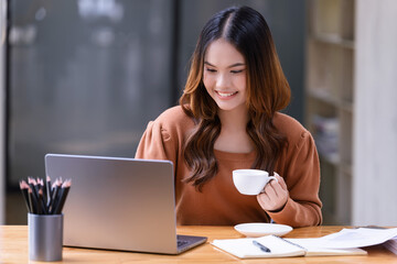 A young woman holding a cup of coffee relaxing sitting at working desk in the office.