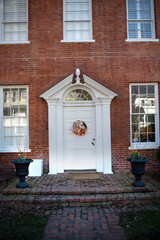 White entrance door to a large brick house with large windows on the facade.