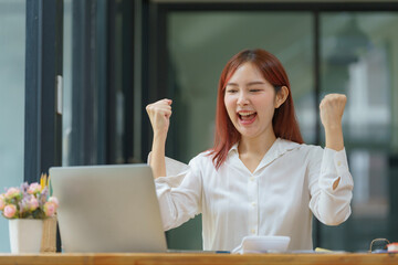 Asian businesswoman cheering while working on a laptop in an office.