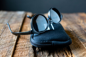 round sunglasses with a case in black plastic frames on textured wood.
