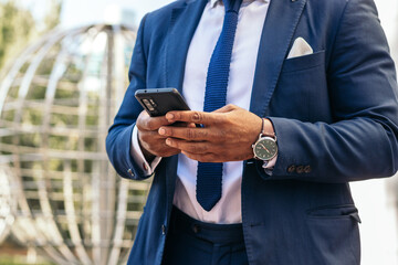Black man in suit using smartphone outdoors