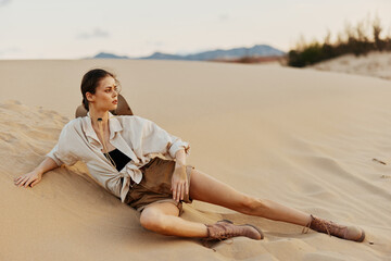 Woman in White Shirt and Shorts Sitting on Top of Sand Dune Enjoying Scenic Desert View