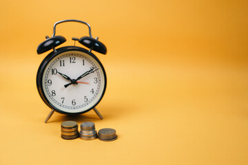 Alarm clock and coins on yellow background. Time is money. Concept of opportunity.