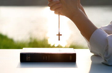 Christian praying, meditating and worshiping with hands together, brightly lit cross and Bible book...