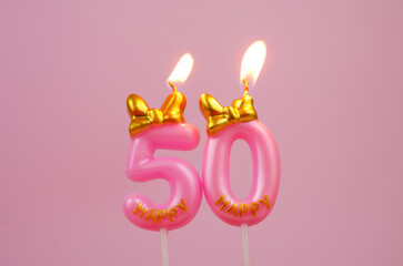Burning pink birthday candle with gold bow and letters happy on pink background. Number 50.	