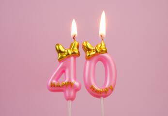 Burning pink birthday candle with gold bow and letters happy on pink background. Number 40.	