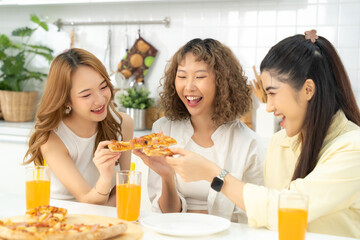 Three friends enjoying a delicious pizza meal together, laughing and drinking orange juice in a sunlit kitchen.