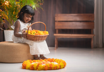 Onam special photo South Indian little girl making Onam pookalam, Cute young girl wearing Kerala traditional dress and holding flower basket