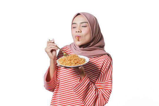 A portrait of a happy Asian woman hijab wearing a red white shirt, eating noodles. Isolated against a white background.