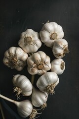 A bunch of garlic bulbs are displayed on a black background. The bulbs are all different sizes and are arranged in a way that they look like a bouquet. Scene is warm and inviting