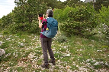 Senior woman standing on the mountain path and taking photo