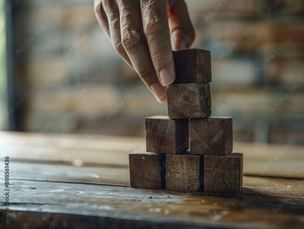 Poster a hand is reaching for a stack of wooden blocks. the blocks are arranged in a pyramid shape, with th