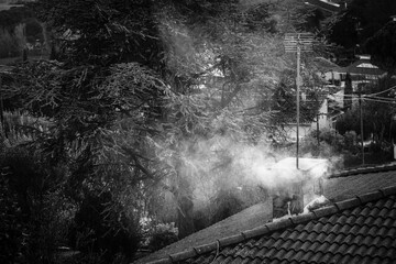 Roof of a house with a chimney releasing smoke into the atmosphere.